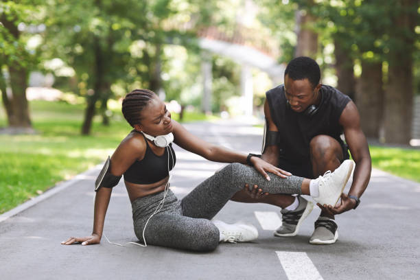 Caring Black Man Massaging Injured Leg Of Girlfriend After Running Together Outdoors, Free Space