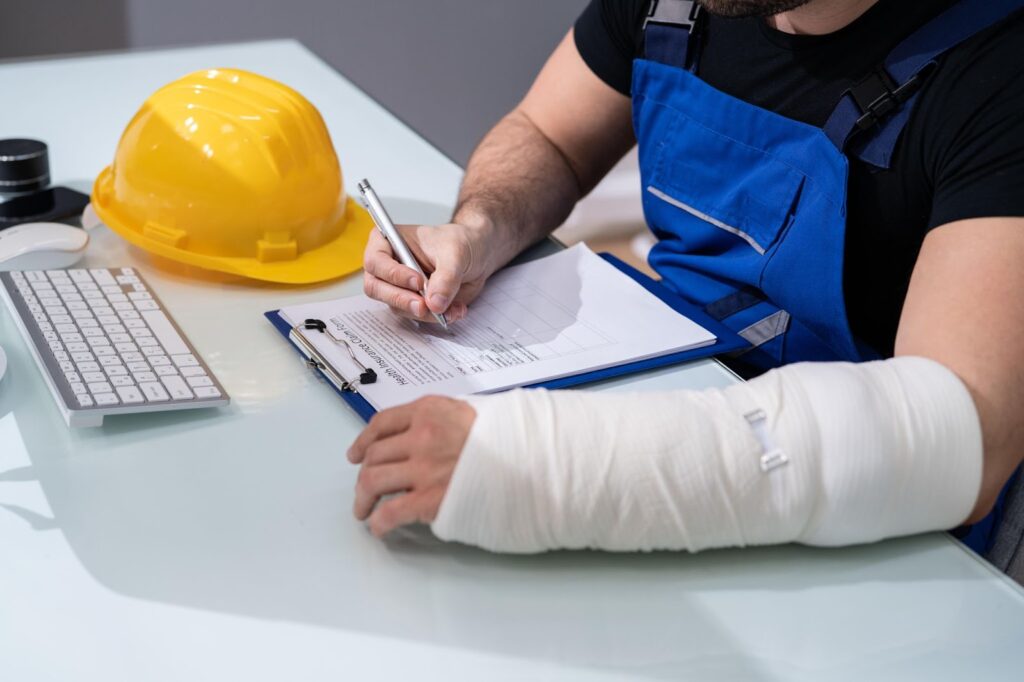Injured worker with arm cast writing notes at desk.