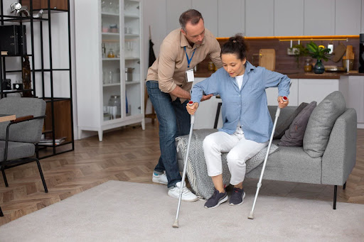 Woman with crutches assisted by a man.