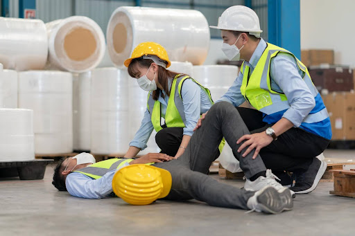 Workers assisting injured colleague in warehouse.