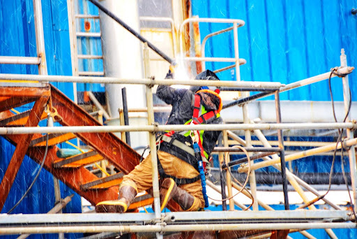Construction worker welding on scaffolding with sparks flying.