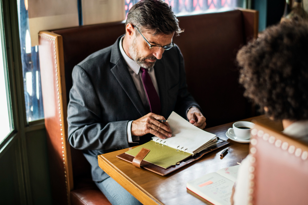 Man in suit writing in a notebook at a cafe.